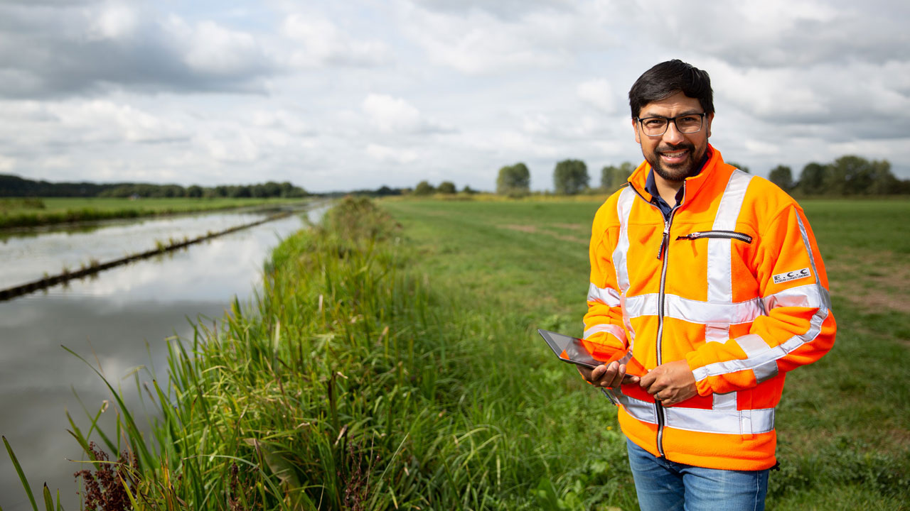 Medewerker met tablet voert veldwerk uit langs watergang, illustratie van dataverzameling en GIS-toepassing met ArcGIS Pro