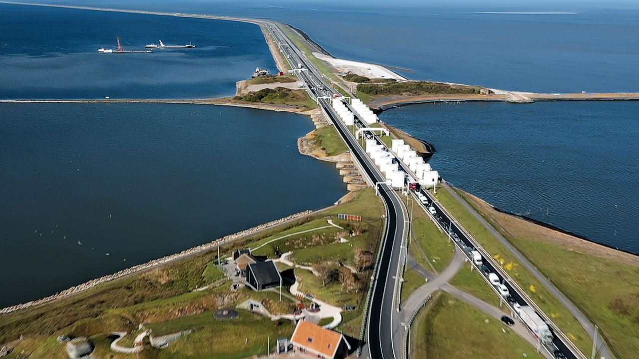 Luchtfoto van waterkering met sluizen en wegen, illustratief voor infrastructuurprojecten in waterbeheer en ruimtelijke ordening