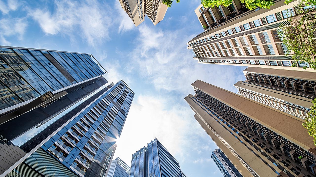 Moderne glazen kantoorgebouwen tegen blauwe lucht, gezien vanaf de grond; focus op stedelijke duurzaamheid en toekomstgericht onderhoud