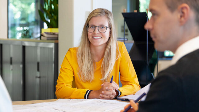 Drie personen in overleg aan tafel met papieren en plannen, in een kantooromgeving gericht op inkoop- en contractmanagement