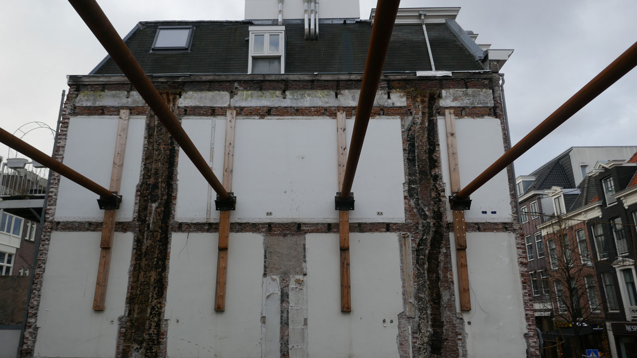 Achterzijde van gebouw in renovatie met zichtbare bakstenen, houten balken en metalen steunconstructie