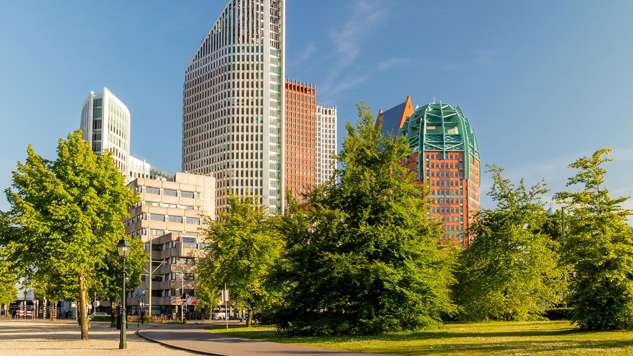 Skyline van Den Haag met moderne torens en veel groen, onder een heldere blauwe lucht – focus op stedelijke duurzaamheid