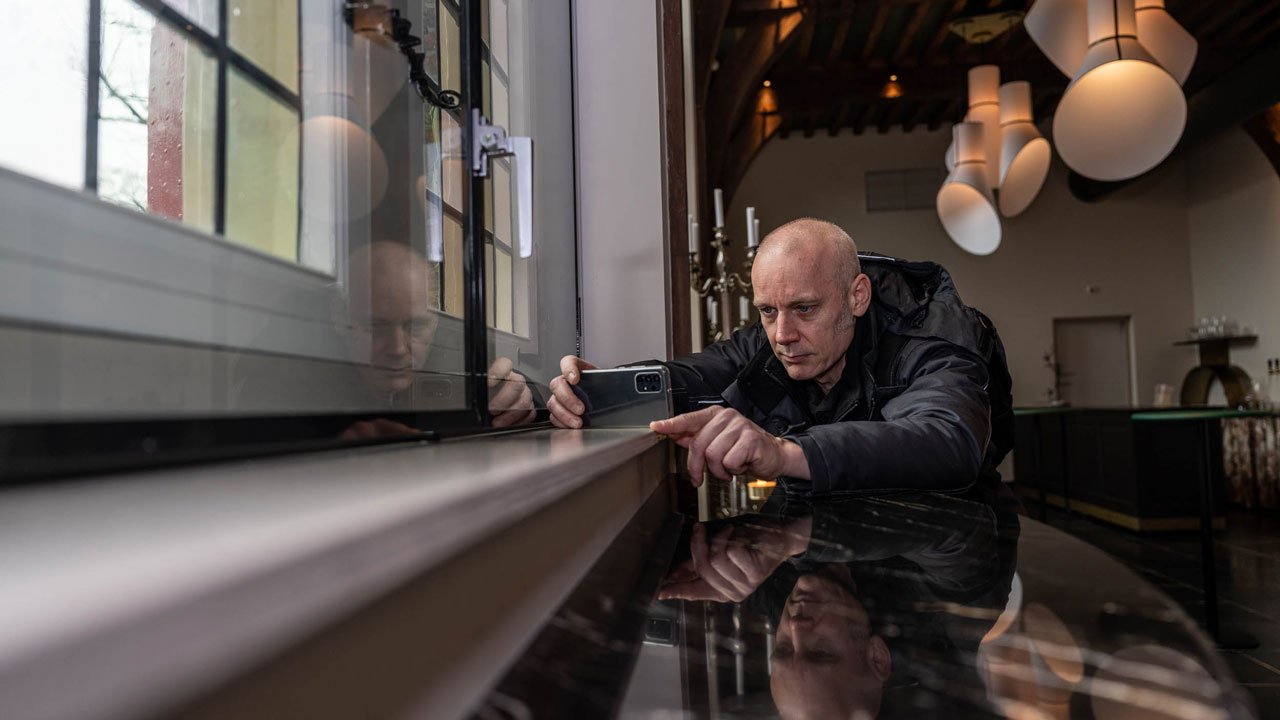 Persoon inspecteert gebouw bij raam, als onderdeel van controle op energiebesparingsplicht en duurzaam vastgoedbeheer