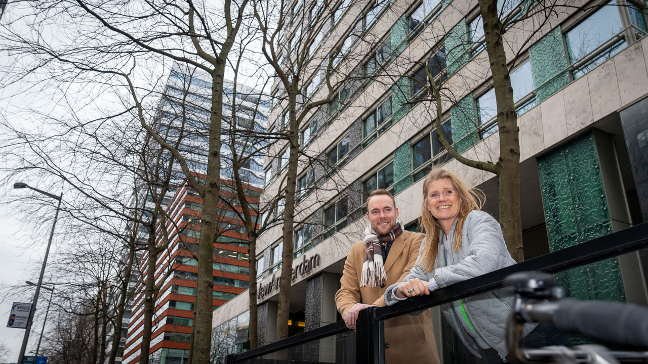 Twee mensen op een brug in een stedelijke omgeving in Rotterdam, met hoge gebouwen op de achtergrond, onderdeel van het Vesteda-project
