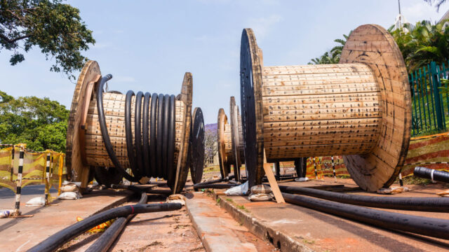 Grote houten kabelhaspels met uitgerolde kabels op verhard terrein, illustratief voor aanleg en verlegging van ondergrondse infrastructuur
