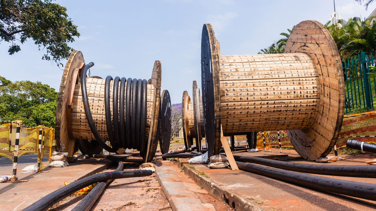Grote houten kabelhaspels met uitgerolde kabels op verhard terrein, illustratief voor aanleg en verlegging van ondergrondse infrastructuur