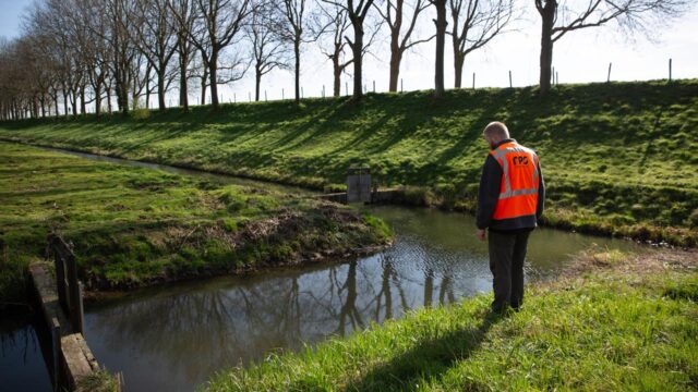 Medewerker bij watergang met grasoevers, voor advies en monitoring in duurzaam waterbeheer