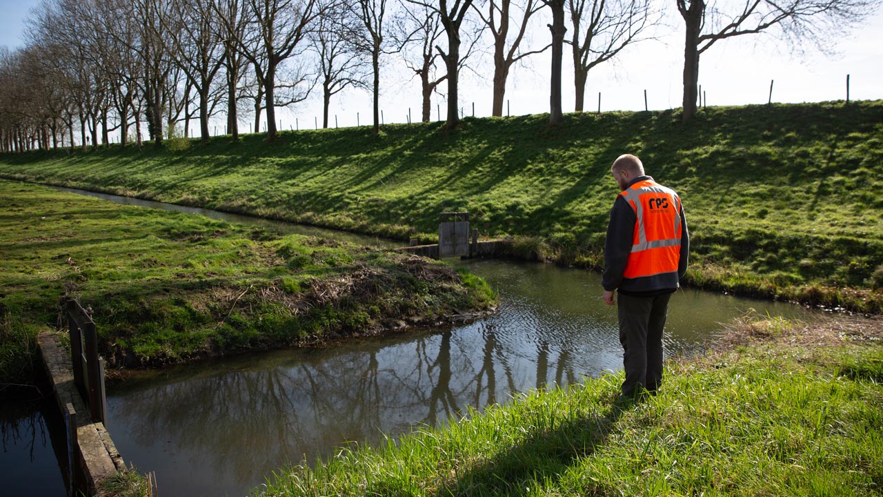 Medewerker bij watergang met grasoevers, voor advies en monitoring in duurzaam waterbeheer