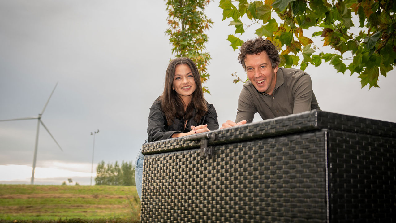 Twee personen bij meetopstelling in buitenomgeving met windturbine op de achtergrond, in het kader van blootstellingsonderzoek.