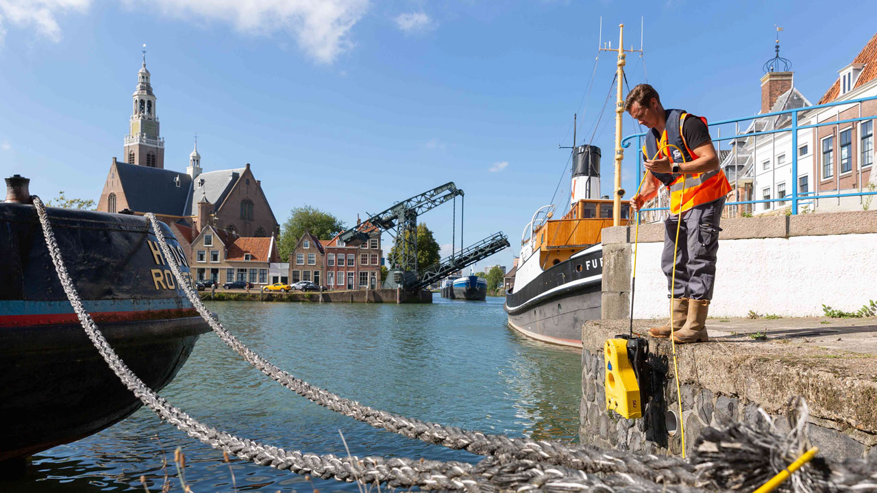Medewerker in veiligheidsvest werkt aan meetapparatuur op kade bij boten en ophaalbrug – maritieme inspecties en veldmetingen in stedelijke omgeving door Tetra Tech Field Services