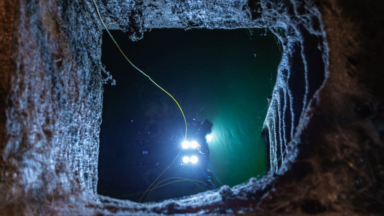 ROV voert onderwaterinspectie uit in donkere ruimte met verlichte apparatuur en kabels