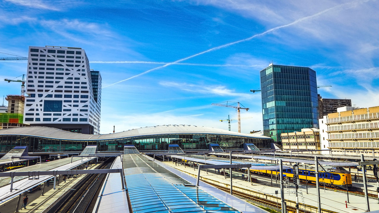 Modern treinstation met meerdere sporen, treinen en bouwkranen op de achtergrond, relevant voor vergunningstrajecten in stedelijke gebieden