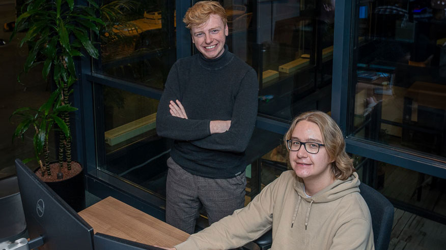 Twee collega's overleggen in kantoor met Dell-monitoren, raamlicht en plant – samenwerking in de energietransitie centraal