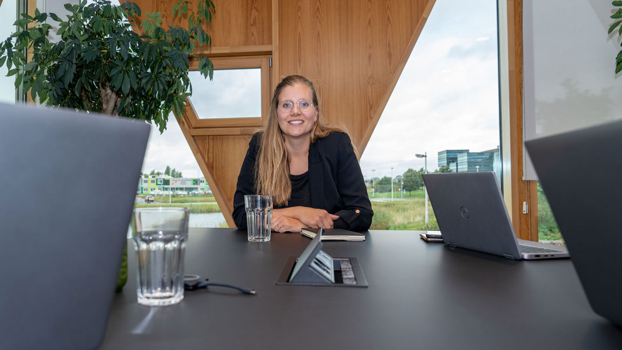 Persoon aan vergadertafel met laptops en uitzicht op groen – overleg en strategie als onderdeel van succesvol aanbesteden