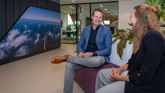 Gesprek in moderne kantoorruimte met scherm vol windmolens, illustratie van visie en duurzaamheid in toekomstgericht vastgoedmanagement