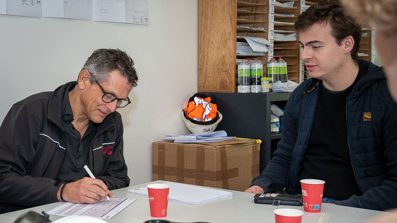 Overleg tussen projectteam met bouwhelm en documenten, illustratie van samenwerking en veiligheid bij duurzaam bouwen in Schiedam