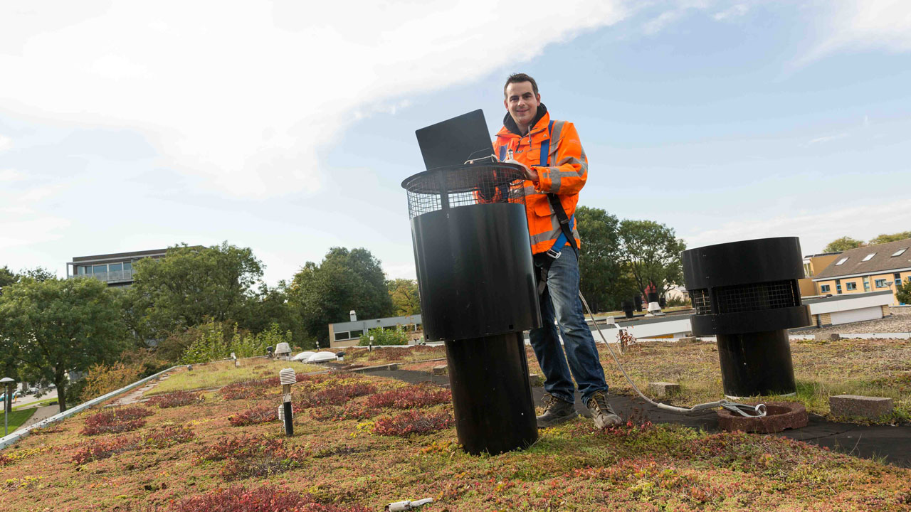 Onderzoeker op groen dak met meetapparatuur, analyseert effect van vegetatie op daken voor hemelwaterafvoer stedelijk klimaat voor gemeente Utrecht