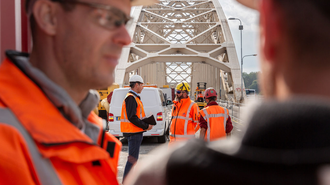 Tetra Tech-team op brug inspecteert civiel kunstwerk voor chroom-6-verwijdering, met veiligheidskleding en materieel in beeld