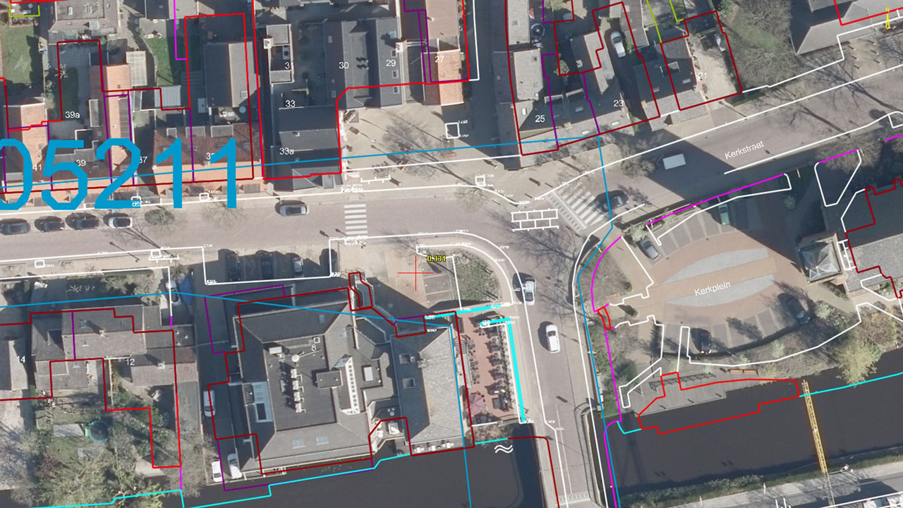 Luchtfoto van een straatkruising met gebouwen en straatnamen, voorzien van gekleurde lijnen die perceelgrenzen of meetgegevens aanduiden. Illustratie van digitale landmeting en geografische data-analyse
