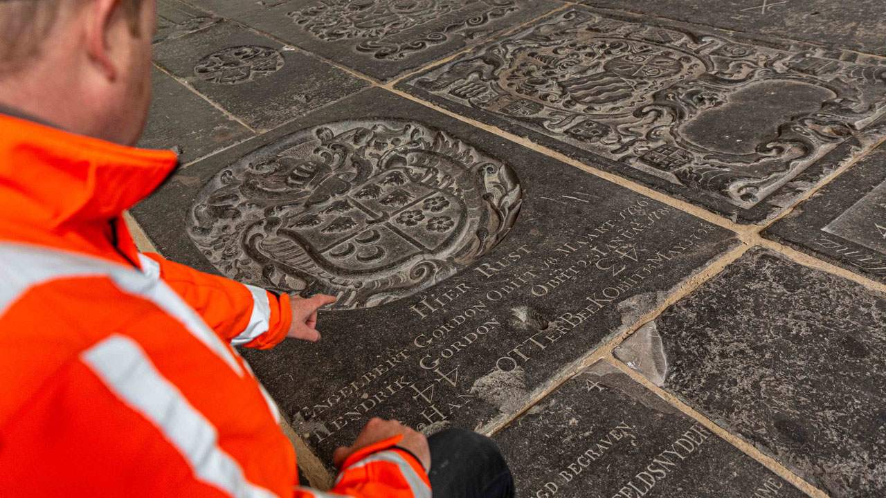 Inspectie van gegraveerde grafsteen in de Oude Kerk Amsterdam, onderdeel van nauwkeurige landmeting en erfgoeddocumentatie