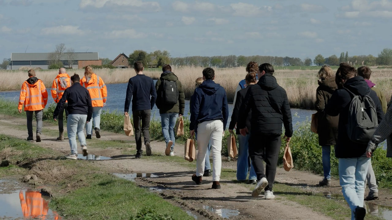Groep wandelt langs water en riet in landelijk gebied – verkenning van ecologische verbindingszones voor natuurontwikkeling