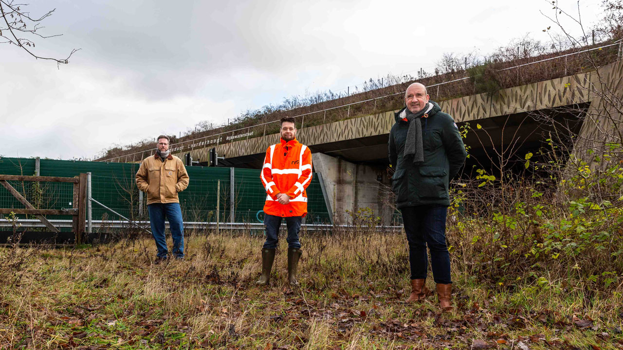 Drie mensen bij natuurbrug in groene omgeving, bevorderen veilige en duurzame verbinding tussen leefgebieden voor mens en dier