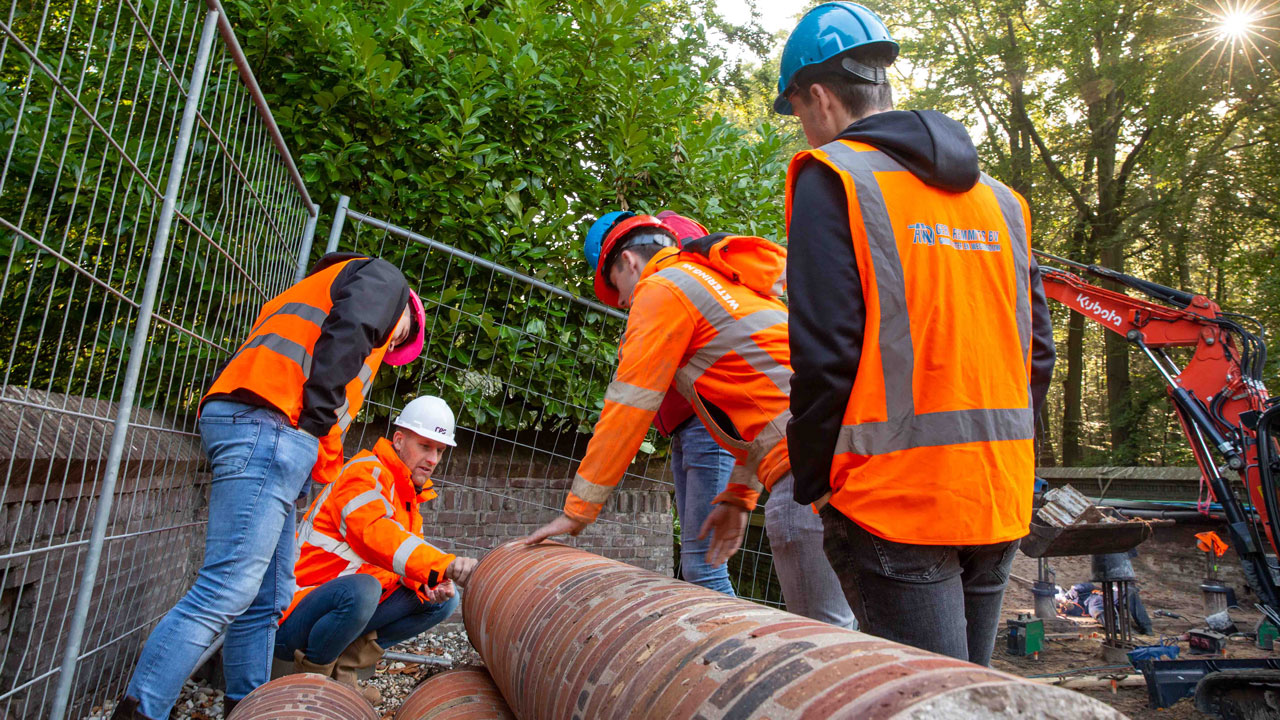 Infra-studenten en vaklieden plaatsen gemetselde buizen bij renovatie boogbrug Naarden – erfgoed en moderne techniek komen samen