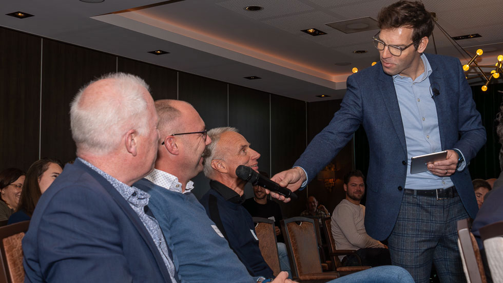 Interactief moment tijdens symposium: deelnemer stelt vraag aan panel in formele setting met publiek
