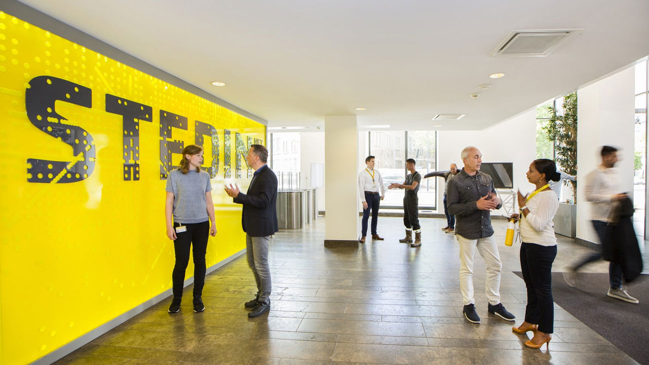 Moderne lobby met mensen in gesprek voor gele wand met 'STERIN', illustratie van samenwerking aan hoogspanningsnetwerk met Tetra Tech