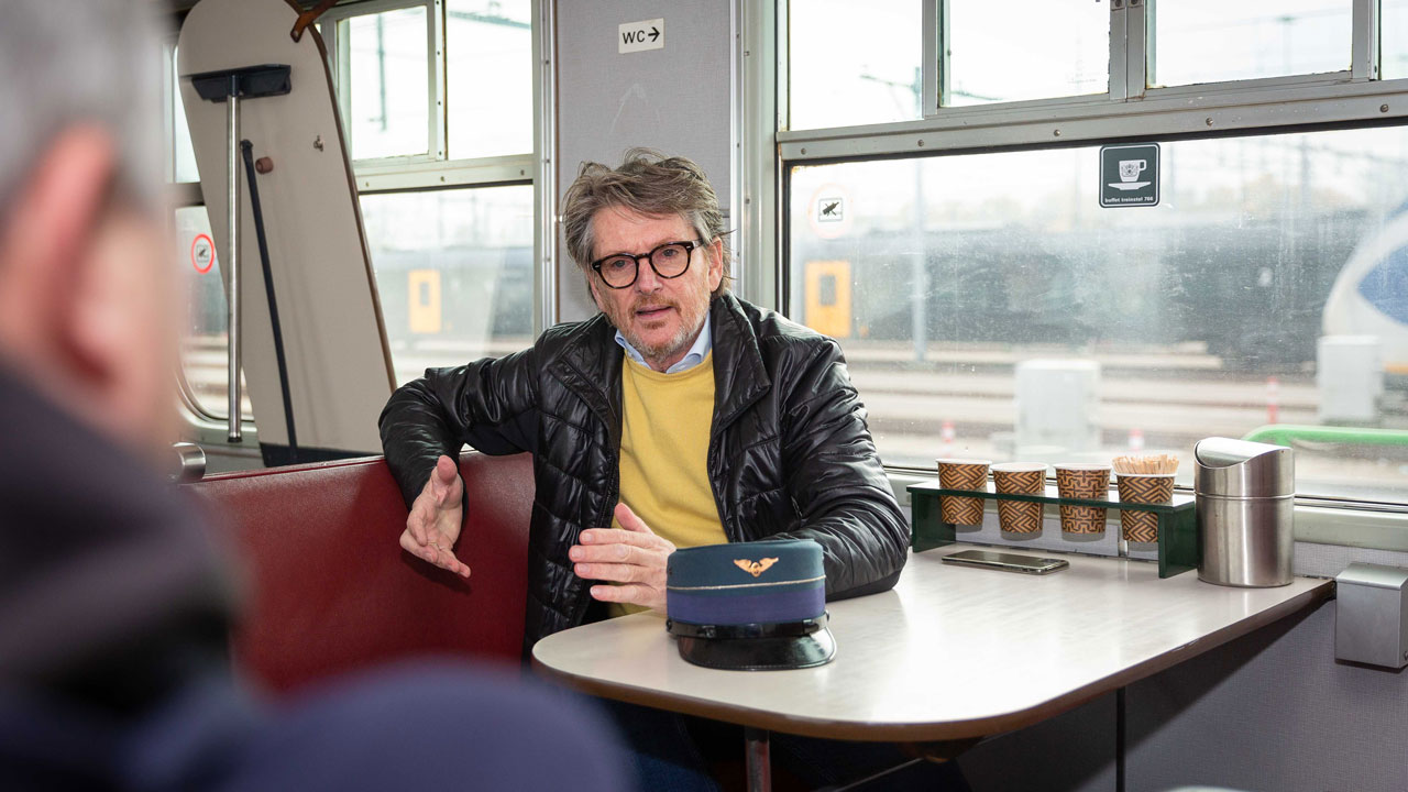 Erik aan tafel in Hondekop-trein met koffiekopjes en WC-bordje