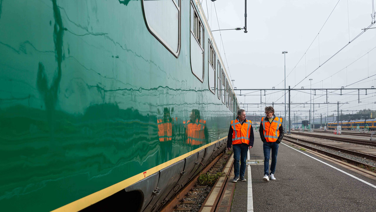 Erik en Herman in oranje hesjes lopen langs groene Hondekop op spoor