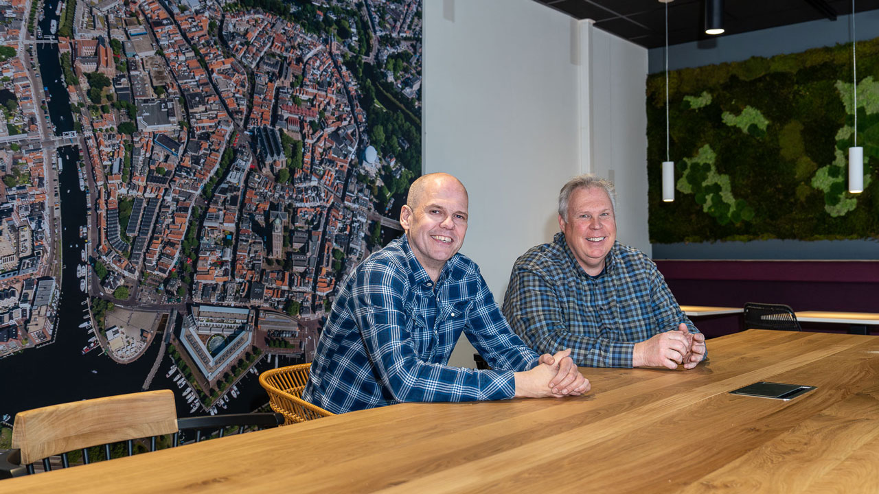 Jacob Steenhuis en Harry Tammes poseren aan houten tafel in nieuwe kantine van het kantoor in Zwolle