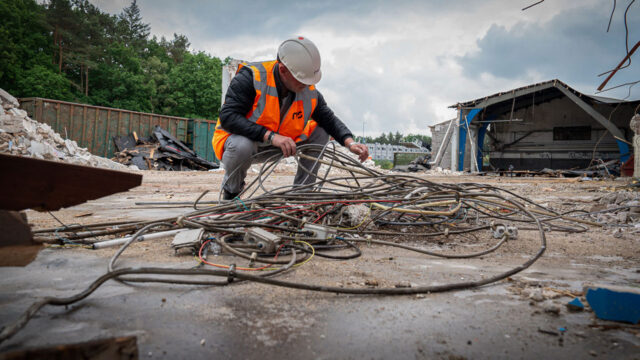 Medewerker werkt tussen puin en kabels op voormalig defensieterrein – voorbereiding op transformatie naar natuurgebied
