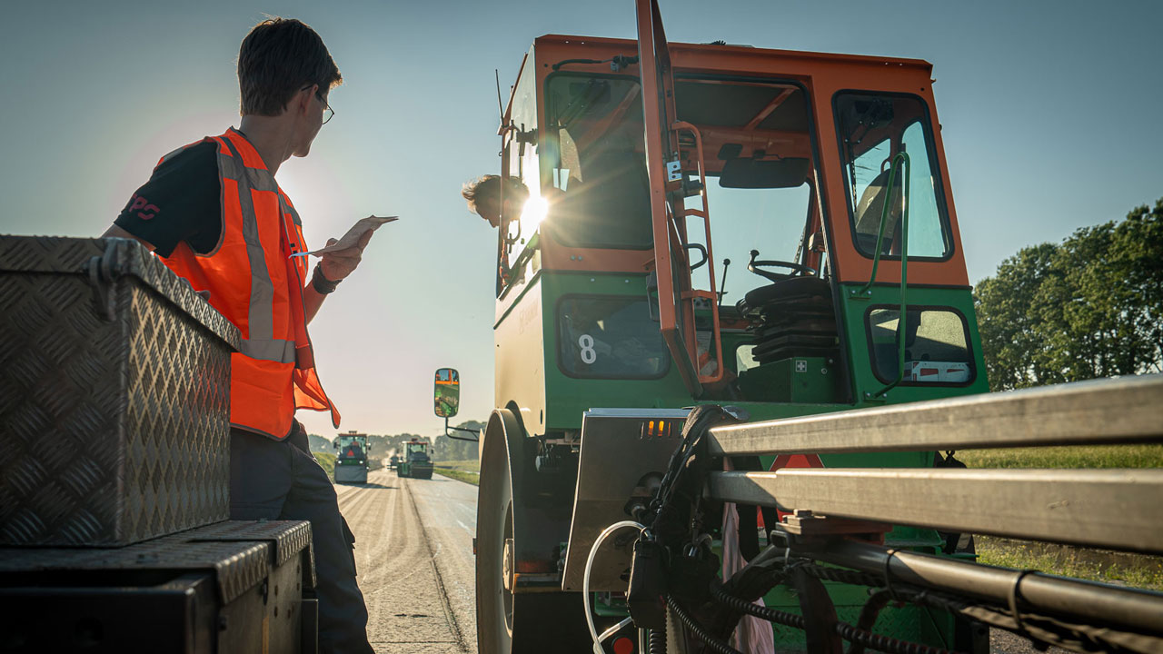 Tetra Tech-medewerker voert metingen voor asfaltrook uit tijdens wegwerkzaamheden, focus op veiligheid en gezondheid bij asfaltprojecten