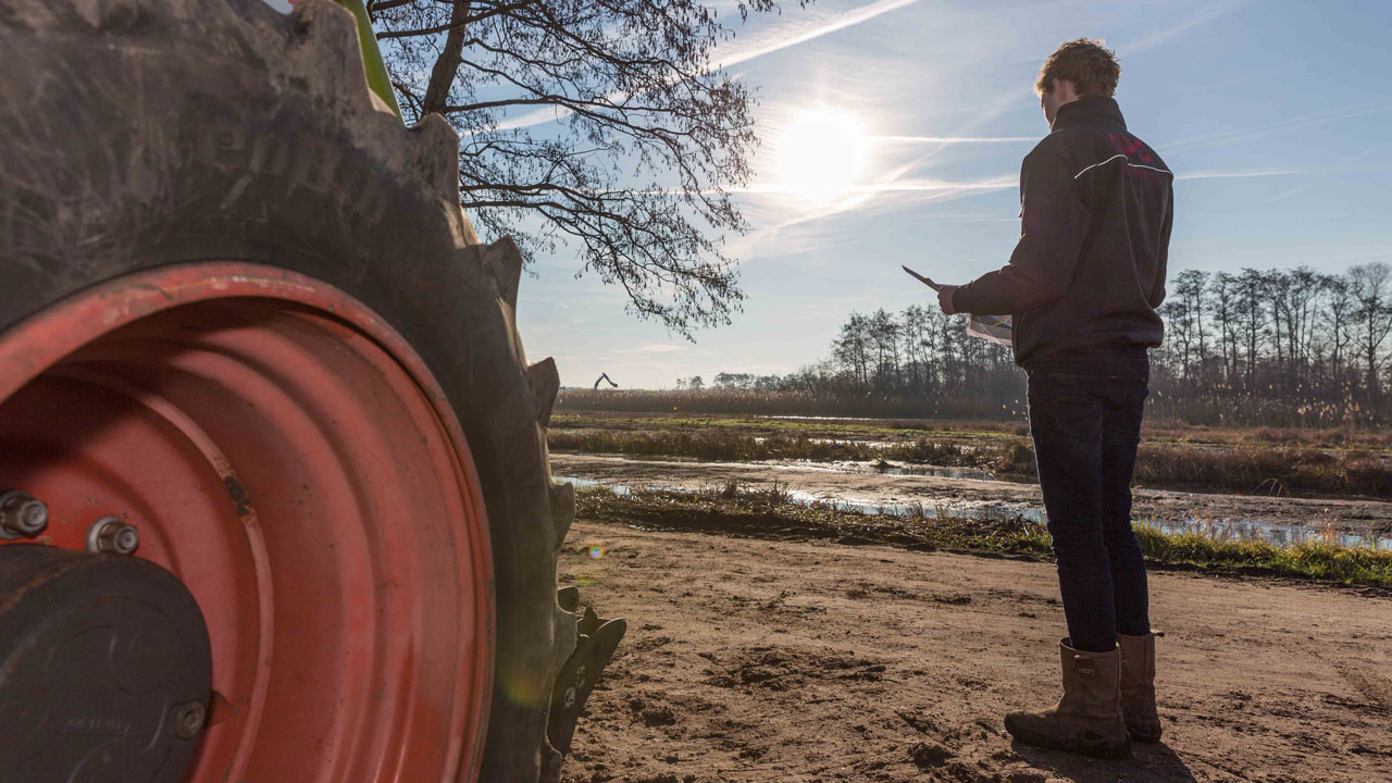 Persoon met tablet bij tractorband in natuurgebied, illustratie van veldwerk en monitoring in de Oostelijke Vechtplassen