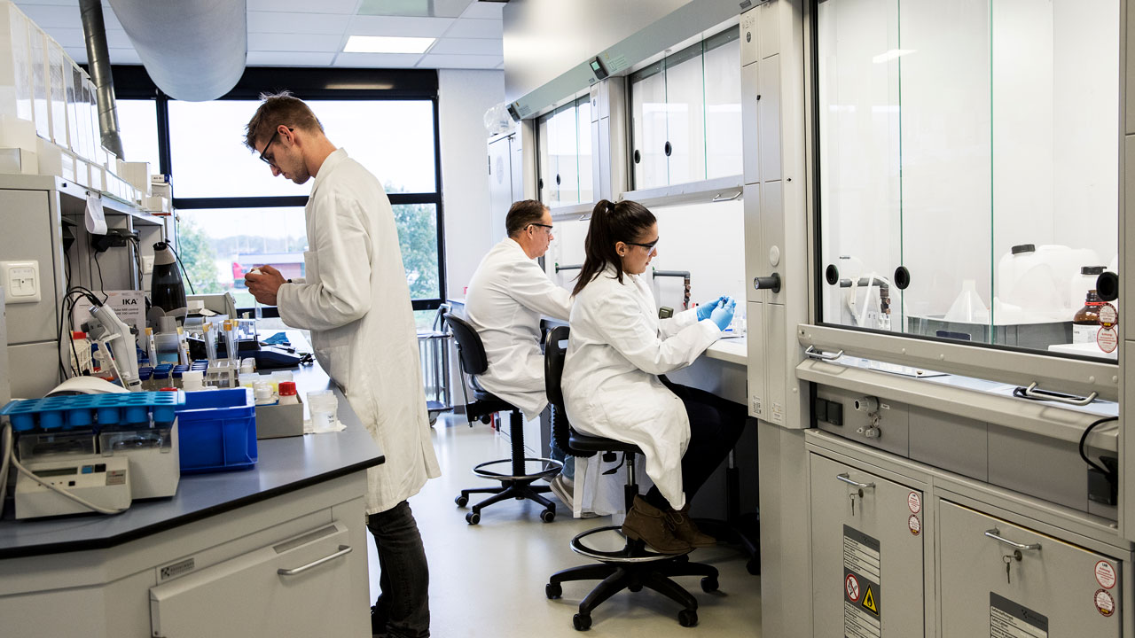 Laboratoriummedewerkers voeren chemische analyses uit onder afzuigkasten in een goed uitgeruste onderzoeksruimte