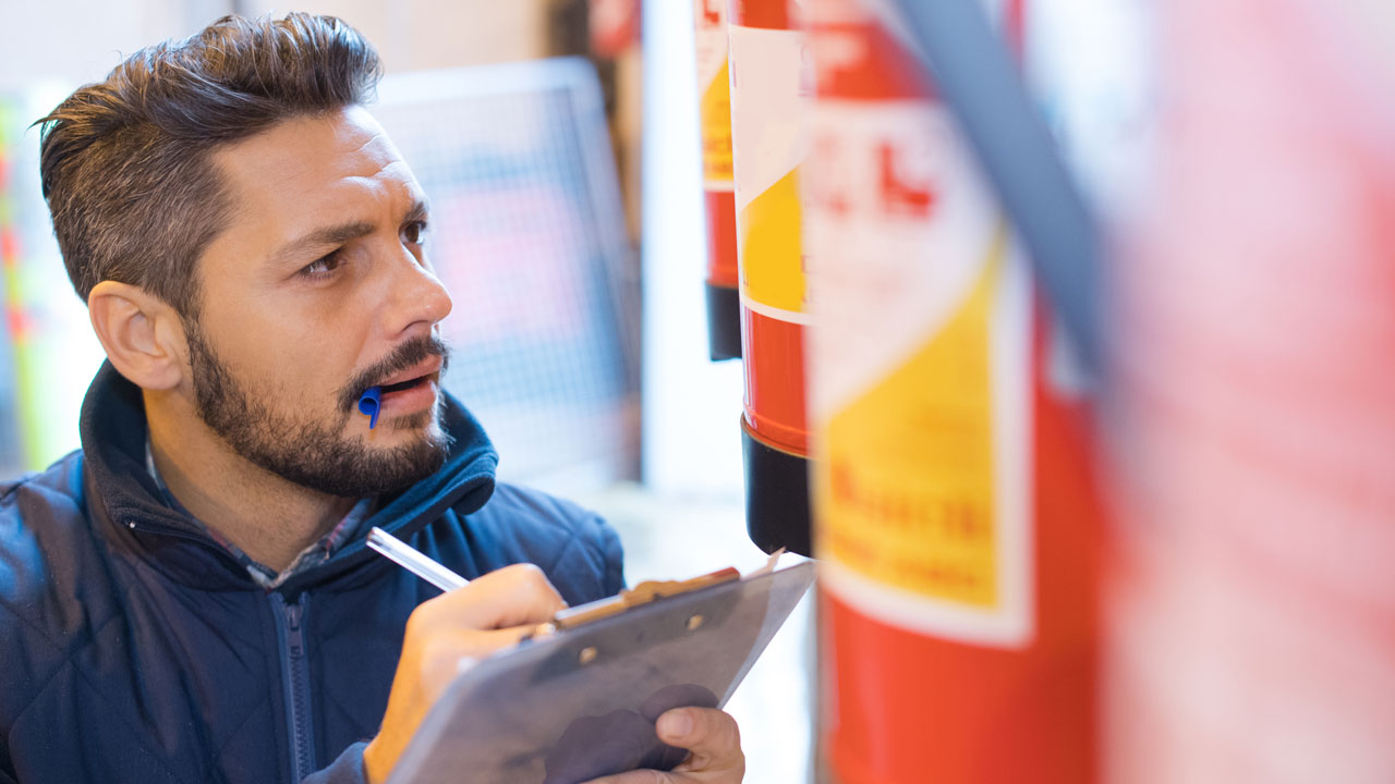 nspecteur controleert brandblussers en noteert bevindingen op een clipboard; meerdere rode blussers staan op een rij opgesteld
