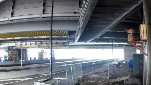 Onderzijde van een brug met zicht op constructieve elementen zoals liggers en steunpunten. Een gemonteerd monitoringapparaat registreert continu de staat van het kunstwerk