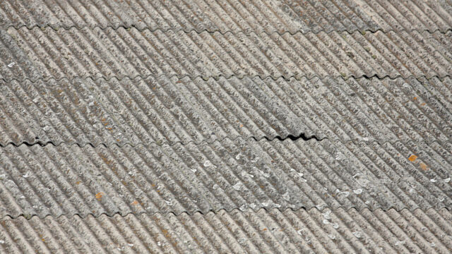 Close-up van een verouderd golfplaten dak met zichtbare vervuiling en slijtage, mogelijk asbesthoudend materiaal