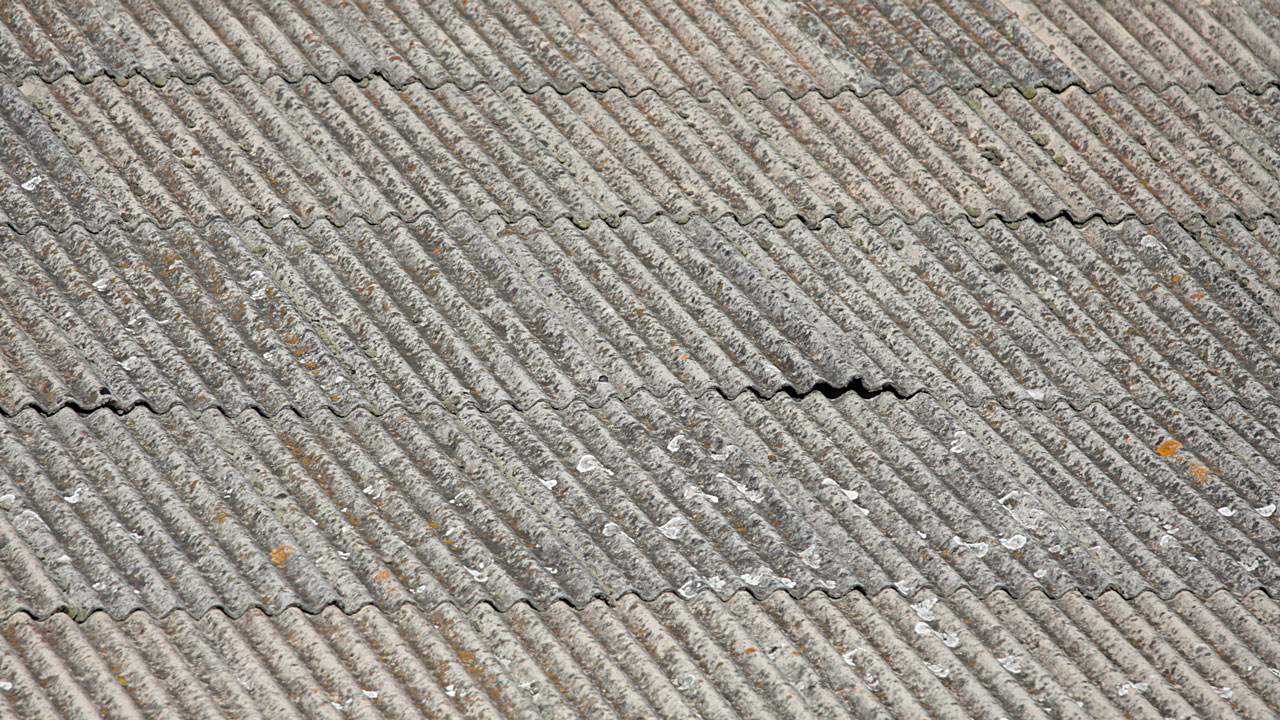 Close-up van een verouderd golfplaten dak met zichtbare vervuiling en slijtage, mogelijk asbesthoudend materiaal