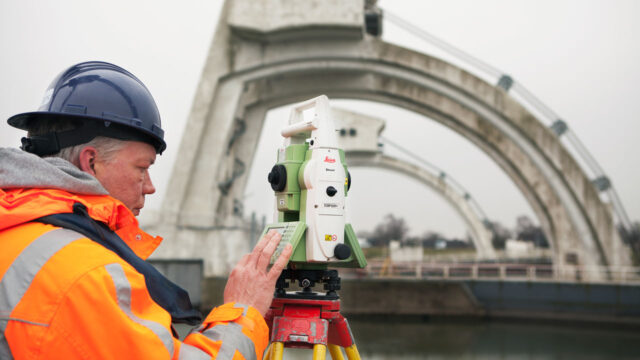 Medewerker met Leica-instrument op statief voert deformatiemetingen uit bij grote betonnen constructie