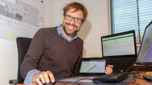 Medewerker analyseert geo-informatie op tablet en meerdere schermen in kantoor met kaart en notities op de muur