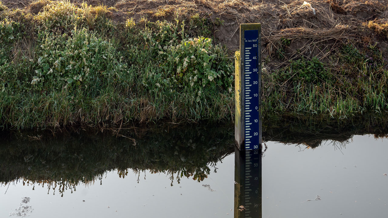 Waterstandsmeter in sloot voor nauwkeurige hoogtemetingen in het veld, gebruikt bij landmeetkundige en hydrologische projecten