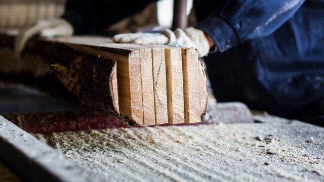 Werknemer verwerkt houten planken in werkruimte met zichtbaar zaagsel, relevant voor blootstelling aan houtstof