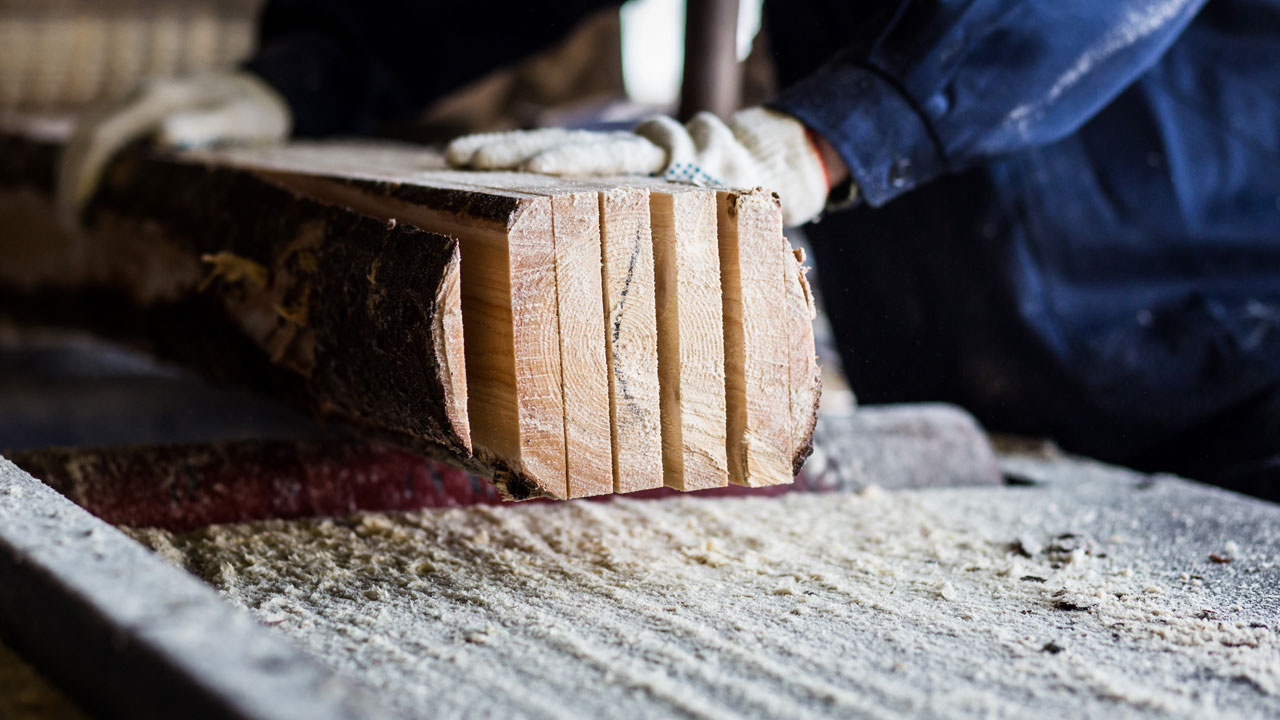 Werknemer verwerkt houten planken in werkruimte met zichtbaar zaagsel, relevant voor blootstelling aan houtstof