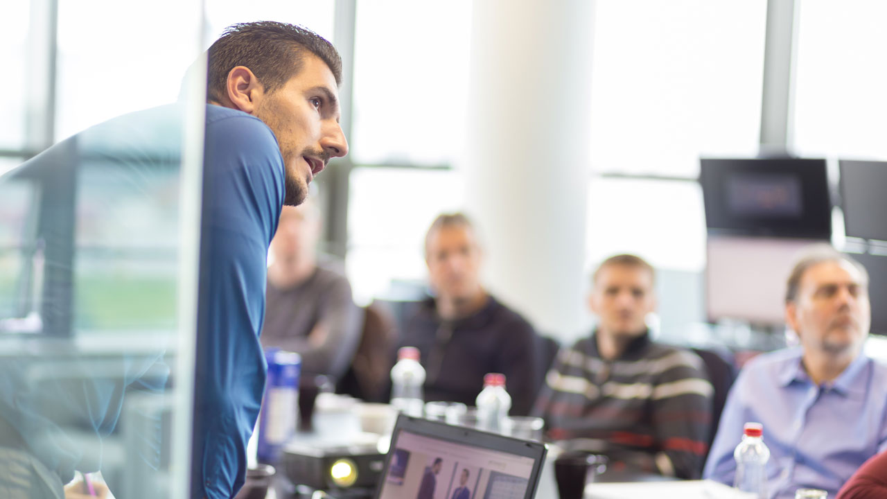 Team bespreekt presentatie over informatiemanagement in vergaderruimte met laptops, schermen en notities op tafel