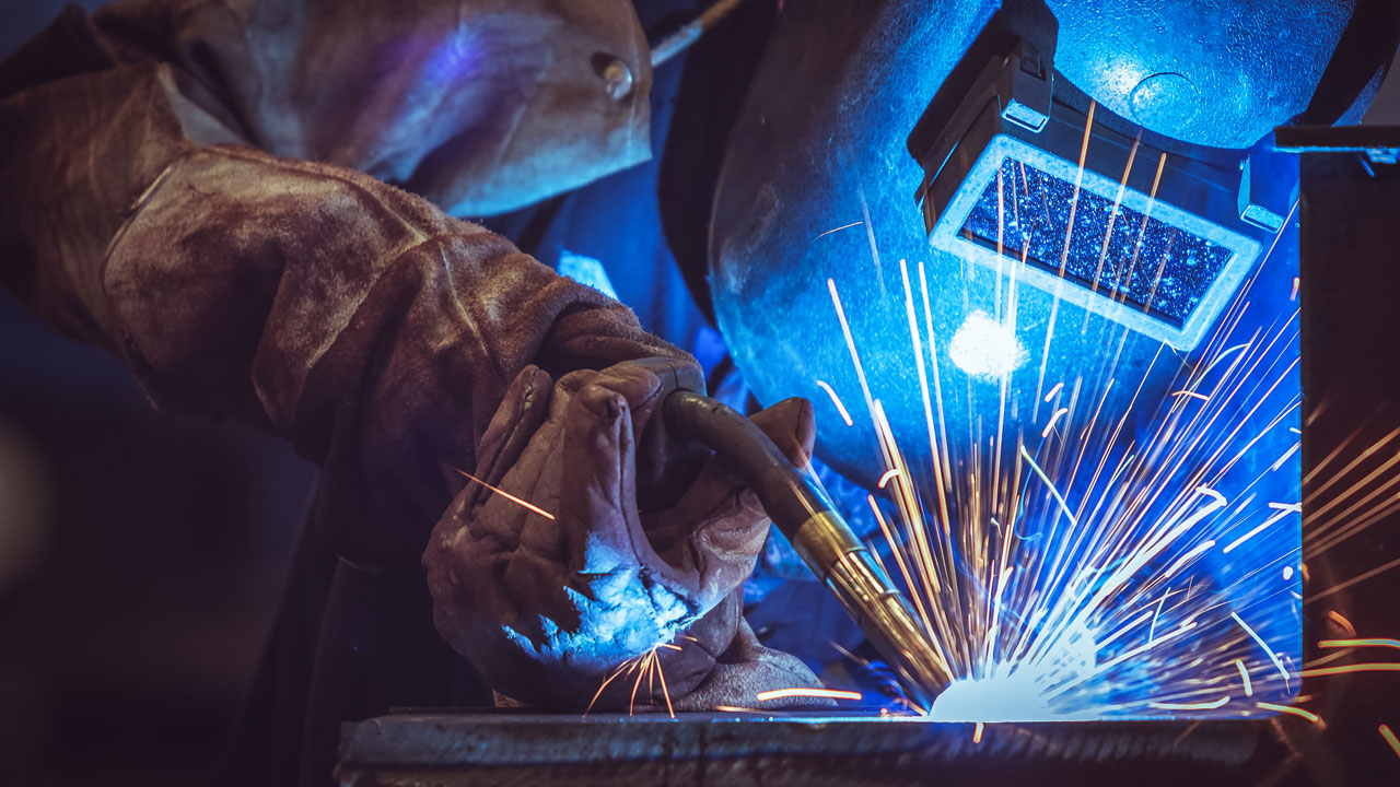Lasser met helm en handschoenen aan het werk – blootstelling aan lasrook en vonken tijdens metaalbewerking