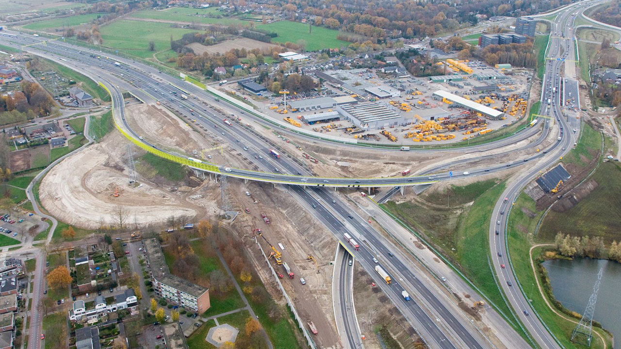 Luchtfoto van knooppunt in aanbouw met wegen, voertuigen en bouwactiviteiten, passend bij maatvoering in infrastructurele projecten