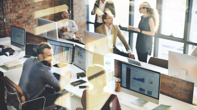 Medewerkers in modern kantoor werken samen aan datarapportages; meerdere schermen tonen grafieken en tabellen in een open, lichte werkomgeving