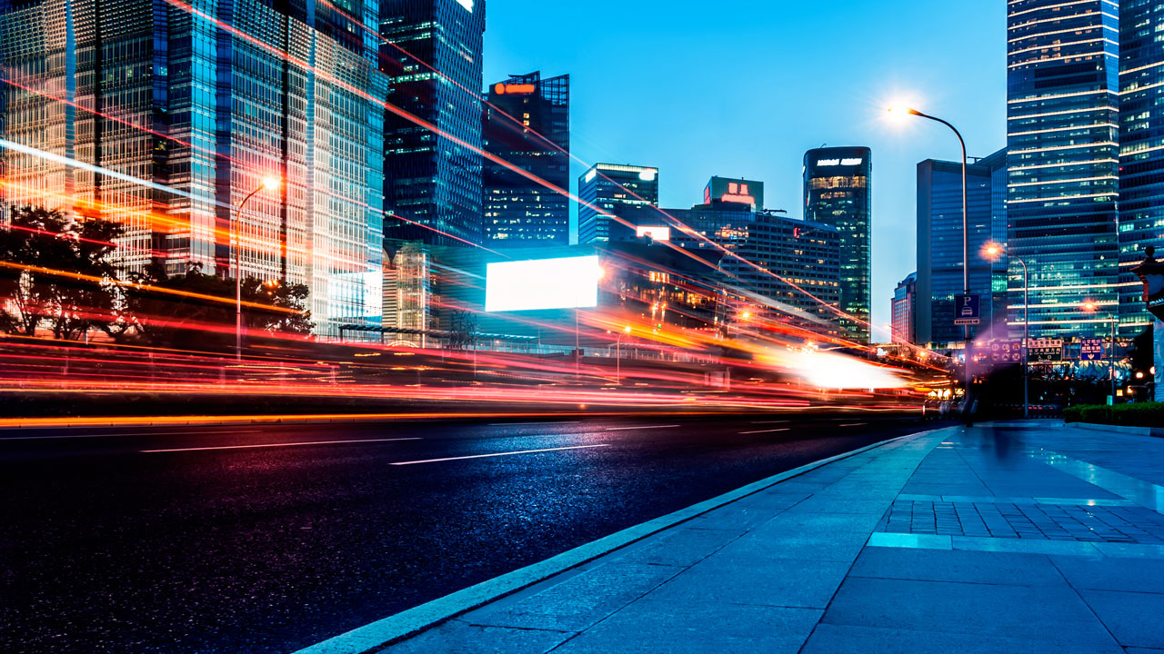 Stadsbeeld bij schemering met lichtsporen van verkeer. Wij borgen kwaliteit en voortgang in stedelijke infraprojecten